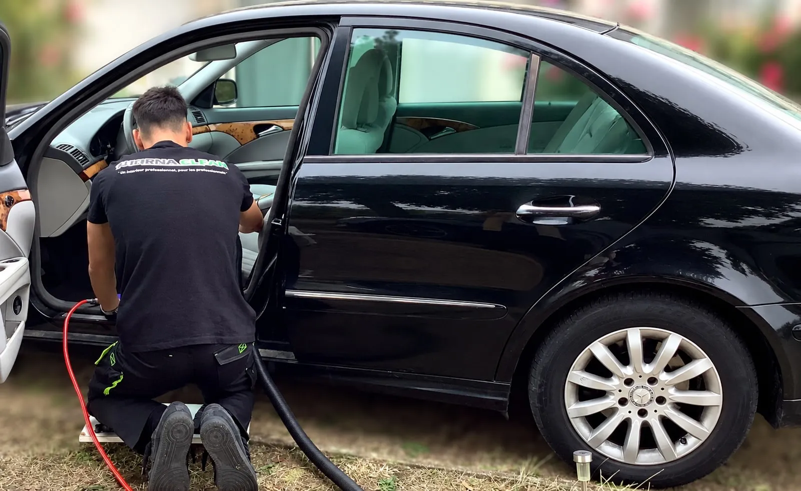 Technicien Thornaclean à genoux nettoyant l’intérieur d’une berline noire, portière ouverte